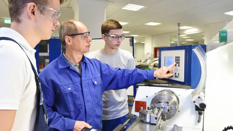 An expert guides trainees on machine operation, showcasing the importance of workforce development consulting in skills training.